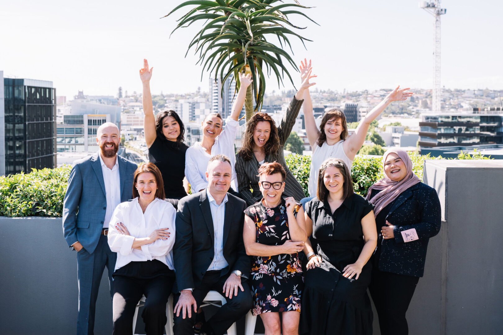 Image of 10 recruitment team members smiling at the top of a rooftop, with the background of Honeysuckle Newcastle behind them