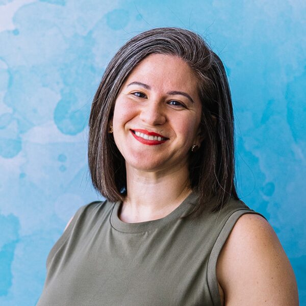 Female Finance manager smiling at the camera wearing a khaki coloured top, red lipstick and straight shoulder length hair.