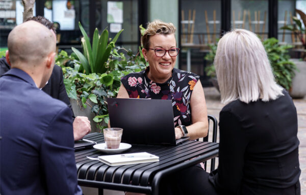 Hiring manager conducting a candidate interview at an outdoor table, discussing the role over a laptop and coffee