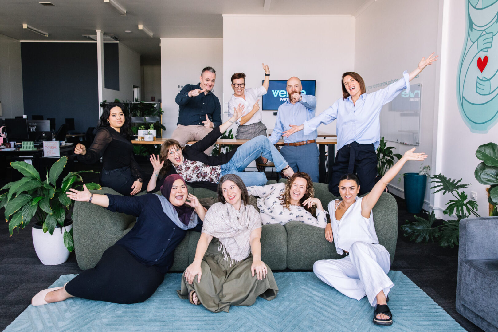 Image of Verve Partners Team, Sitting on Green Lounge in Office located in Hamilton, Newcastle. Team are smiling with hands in air, showing joy